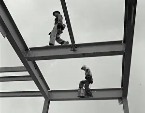 Construction Workers Imprime: Two construction workers walking on the frame of a grain elevator