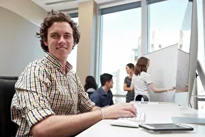 Office Communication Skills Imprime: Young man using computer in office looking towards camera