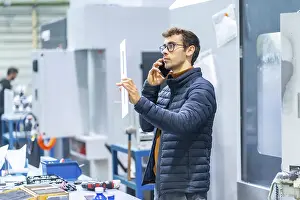 Communicative Young Adult Man Imprime: Engineer talking to the mobile in a computer numeric control factory