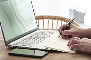 Man Working From Home Imprime: man taking notes on paper while using laptop computer