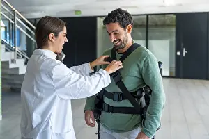 Mechanical Exoskeleton Imprime: Mechanical exoskeleton, female physiotherapist doctor putting tapes on disabled person with robotic skeleton