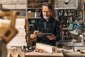 Senior Carpenter Imprime: Senior carpenter using a digital tablet in his workshop