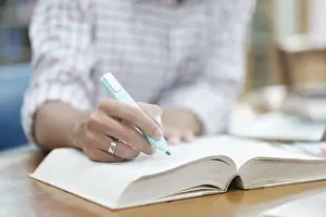 Laptop Computer Use Imprime: A student writes notes in a notebook while studying in a library