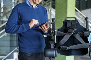 Exoskeleton Technology Imprime: Unrecognizable computer engineer in mechanical exoskeleton looking at the robot with a tablet