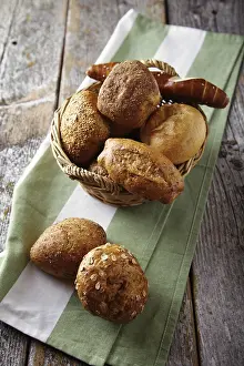 Freshly Baked Goods Imprime: Various types of bread in a basket lying on a rustic table