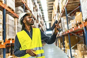 Supply Chain Management Imprime: Side view of an african worker scanning package with bar code reader in a distribution warehouse